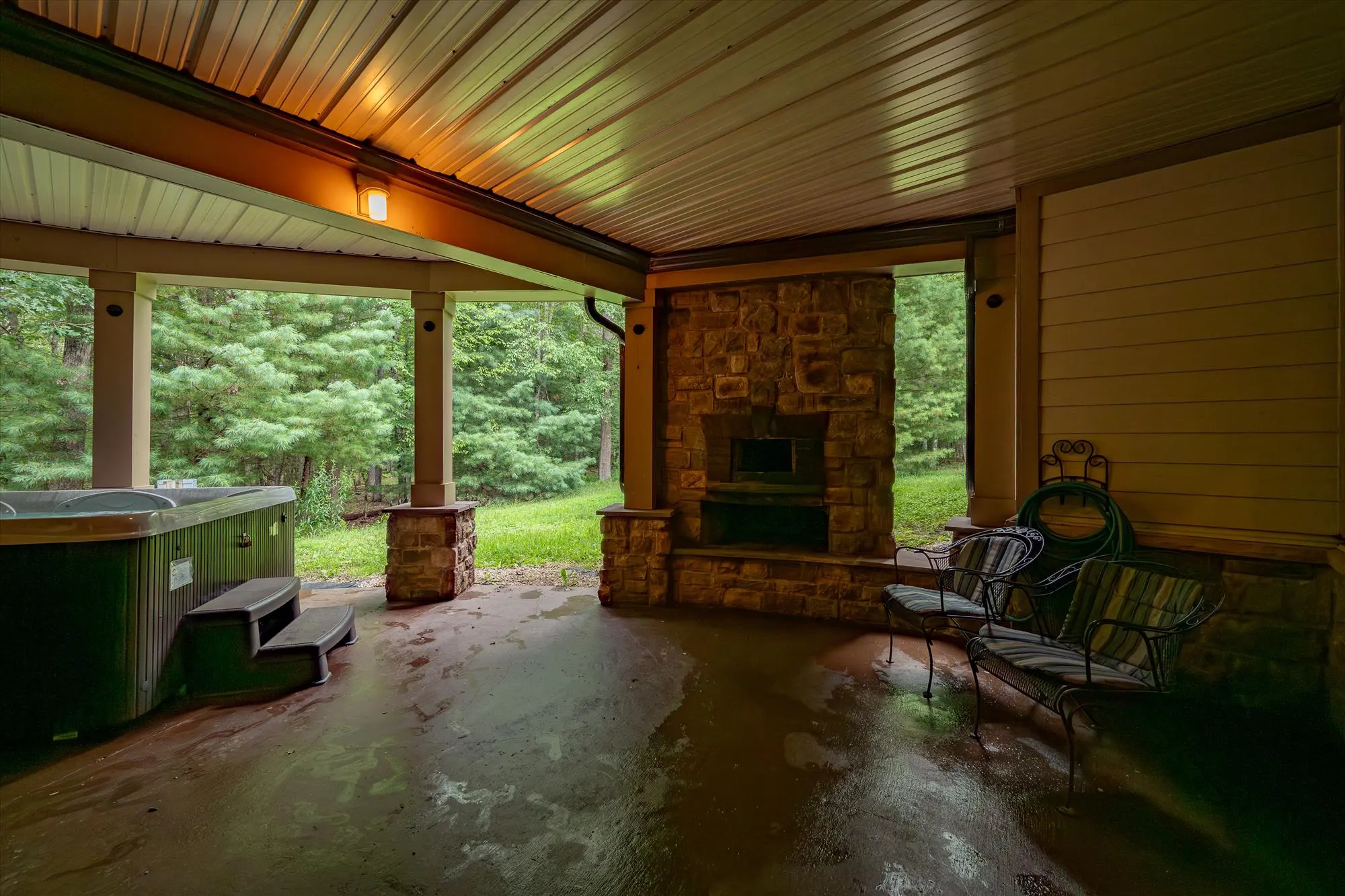 Stone patio on the lower level with outdoor fireplace and woodland backdrop